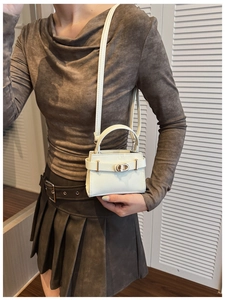 Detail of a creamy white mini crossbody bag with gold turn-lock and pebbled leather texture