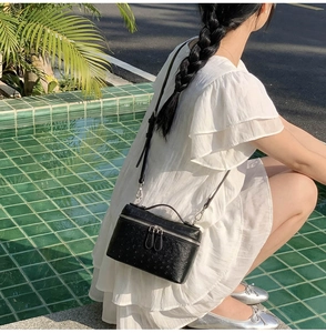 Close-up of black ostrich pattern crossbody box bag worn with a white summer dress