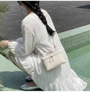 Chic cream box-shaped crossbody bag worn by a model in a casual outdoor setting