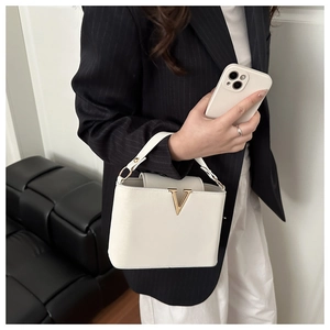 Close-up of a white PU leather handbag with a prominent golden V-shaped metal buckle detail