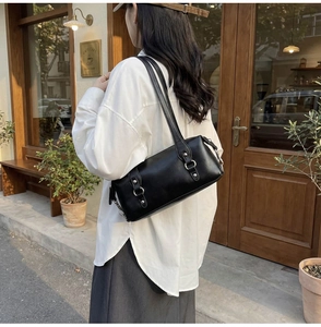 Vista laterale di una borsa sottobraccio vintage in pelle nera con dettagli in argento su modella