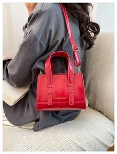 Close-up of a glossy red crossbody bag featuring gold lettering and adjustable strap