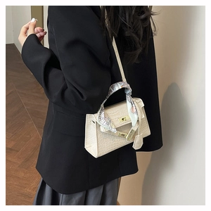 Detail of beige crocodile embossed handbag with printed silk scarf on the top handle