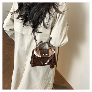 Detail of dark brown croc-embossed handbag with gold clasp and silk scarf handle decor