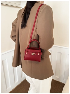 Sac bandoulière moderne en cuir rouge avec boucle dorée sur un costume marron