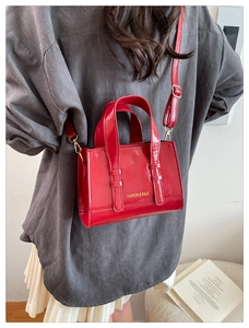 Rear view of a model wearing a glossy red patent leather rectangular crossbody handbag
