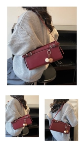Detail of burgundy leather baguette bag with silver ring and plush charms on grey sweater