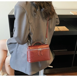 Detail of burgundy ostrich texture vanity bag with silver hardware on a crossbody strap