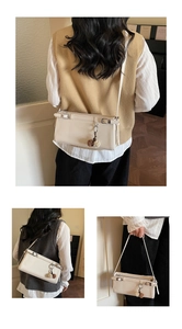 Detail of cream white baguette bag featuring a metal buckle strap and plush pompom charm