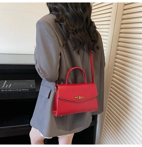 Detailed view of red crossbody bag with metal twist lock worn with gray suit