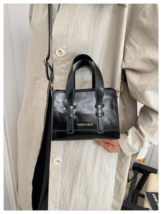 Detail of black wax leather handbag with gold metal hardware and adjustable shoulder strap