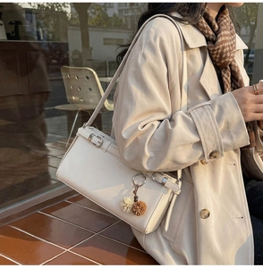 Detail of minimalist beige shoulder bag with metal buckle and decorative plush charms