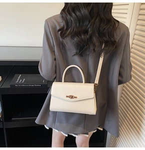Modern cream shoulder bag with spindle lock worn with a dark grey blazer by a model
