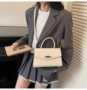 Chic beige crossbody bag with gold lock shown on model wearing grey blazer