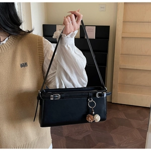 Detail of black square shoulder bag with silver buckles and two-tone plush pompom charm