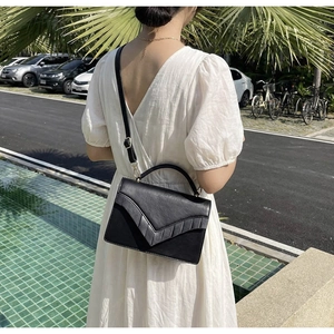 Detail of a chic black crossbody bag with V-shaped textured flap on a white dress