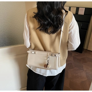Minimalist beige crossbody bag shown on a model with a stylish pompom keychain
