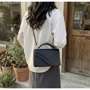 Detail of a black textured leather crossbody bag with V-shaped flap on a street background
