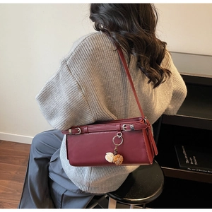 Detail of a dark red matte leather shoulder bag with silver buckles and pompom charm