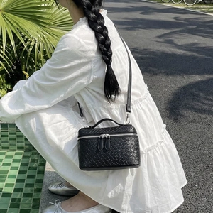 Elegant black woven leather vanity bag with top handle and crossbody strap in outdoor setting