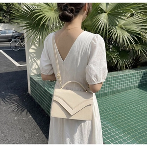 Fashionable cream white PU leather handbag with V-shaped flap design shown in outdoor scene