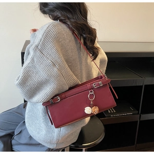 Detail view of burgundy square underarm bag with silver buckle and plush ball charm