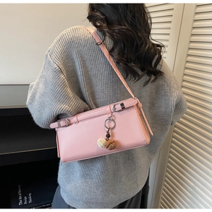 Pink faux leather baguette bag shown on shoulder with pompom charm and buckle detail