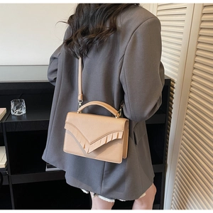 Chic beige textured faux leather handbag with wavy fringe detail worn over the shoulder