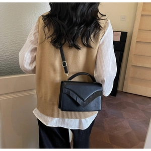 Detailed view of black flap bag with V-shaped design and gold hardware on model