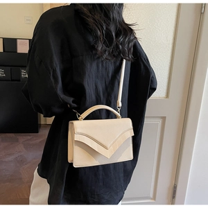 Detail of cream V-shaped flap handbag worn as a stylish crossbody bag with top handle