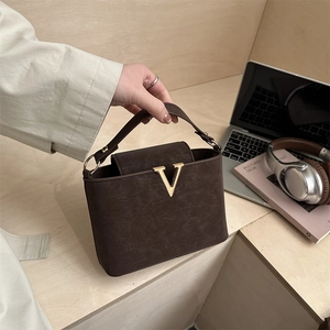 Elegant dark brown leather tote bag with gold V detail on a wooden desk setting