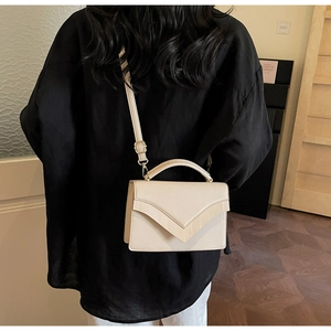 Detail of a chic cream crossbody bag with V-shaped flap design worn by a model