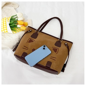 Détail du sac cabas bicolore avec motif de chat à côté d'un smartphone pour l'échelle de taille