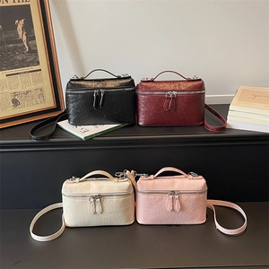 Chic ostrich-textured box handbags in four colors displayed on a podium with accessories