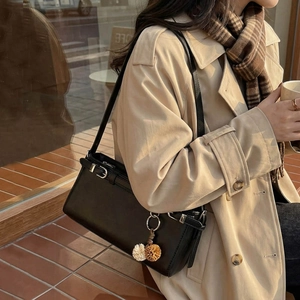 Minimalist black square crossbody bag with metallic buckle and plush charm detail