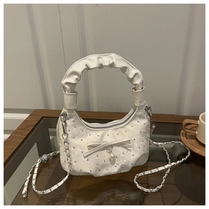 Close-up of white pleated moon bag featuring metallic studs, a bow and pearl charm