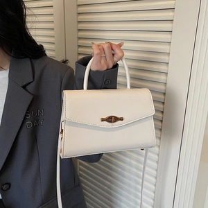 Minimalist white leather crossbody bag with vintage bronze lock held by a model in a suit