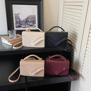 Women's V-shaped textured leather handbag in four colors shown on a stylish wooden shelf