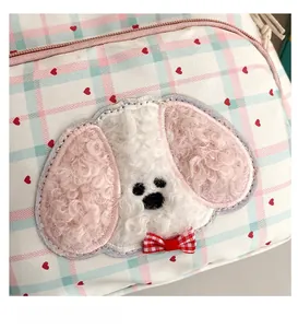 Close-up of pink and blue checkered backpack featuring a cute plush dog patch detail
