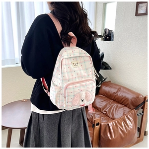 Detail of pink plaid backpack with plush puppy patch worn by model in cozy room