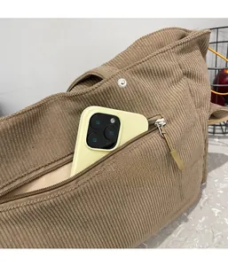 Dettaglio borsa tote in velluto marrone con tasca laterale a zip che contiene un cellulare