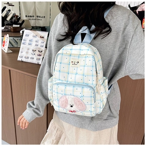 Blue plaid school backpack with plush puppy patch shown on a model in a cafe setting