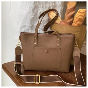 Detail of dark brown leather tote bag showing grainy texture and chic woven strap on a desk