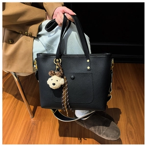 Detail of black pebbled leather tote bag with gold rings and plush puppy charm