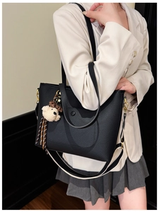 Detail of black lychee grain tote bag with striped strap and bear charm decoration