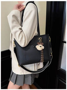 Detail of black pebbled leather tote bag with striped strap and plush bear charm