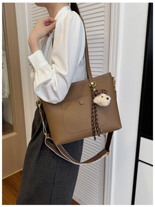 Detail of brown litchi pattern leather tote bag with plush dog charm and woven strap