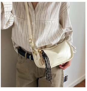 Detail of a beige cylindrical crossbody bag with woven tassel and gold tennis racket charm