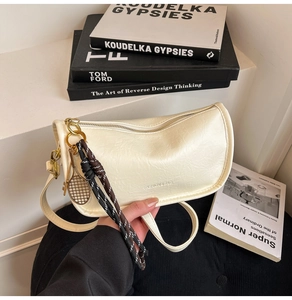 Detail view of beige curved tote bag featuring golden racket charm and woven cord accents