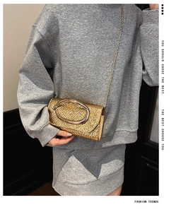 Close-up of metallic gold chain bag featuring a large oval buckle and crinkled texture